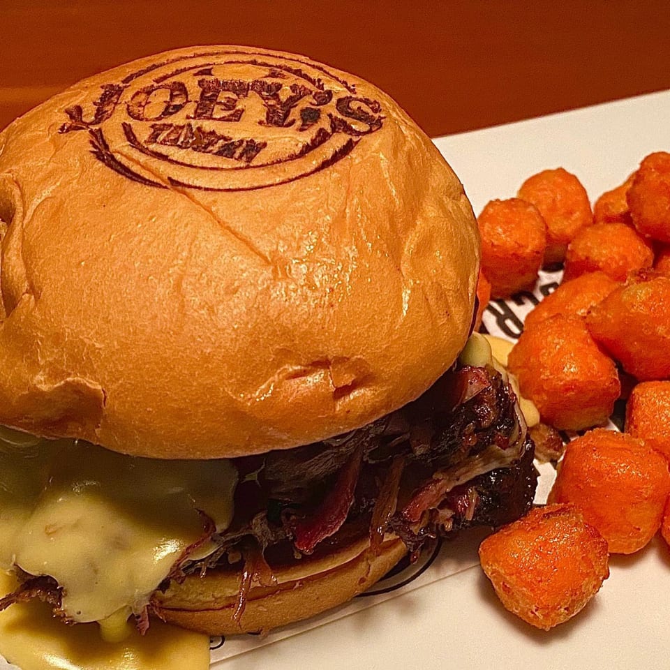 A Joey's Tavern burger with melted cheese and caramelized onions, served with a side of tater tots.