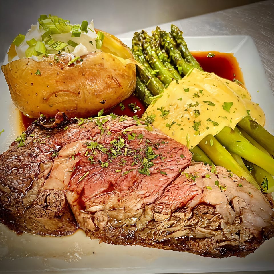 Joey's Tavern prime rib with a baked potato, asparagus, and cheese sauce on a white plate.