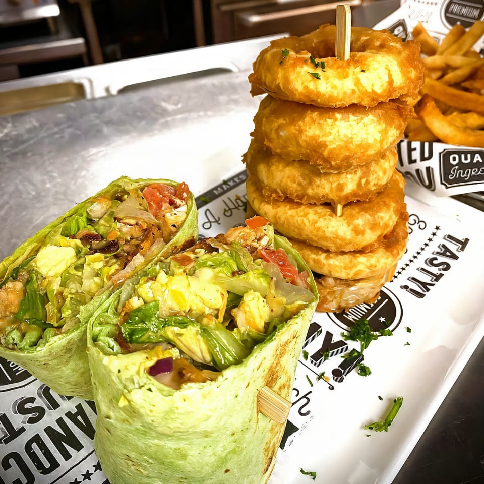 Two green wraps filled with salad and chicken, alongside a tall stack of golden onion rings.
